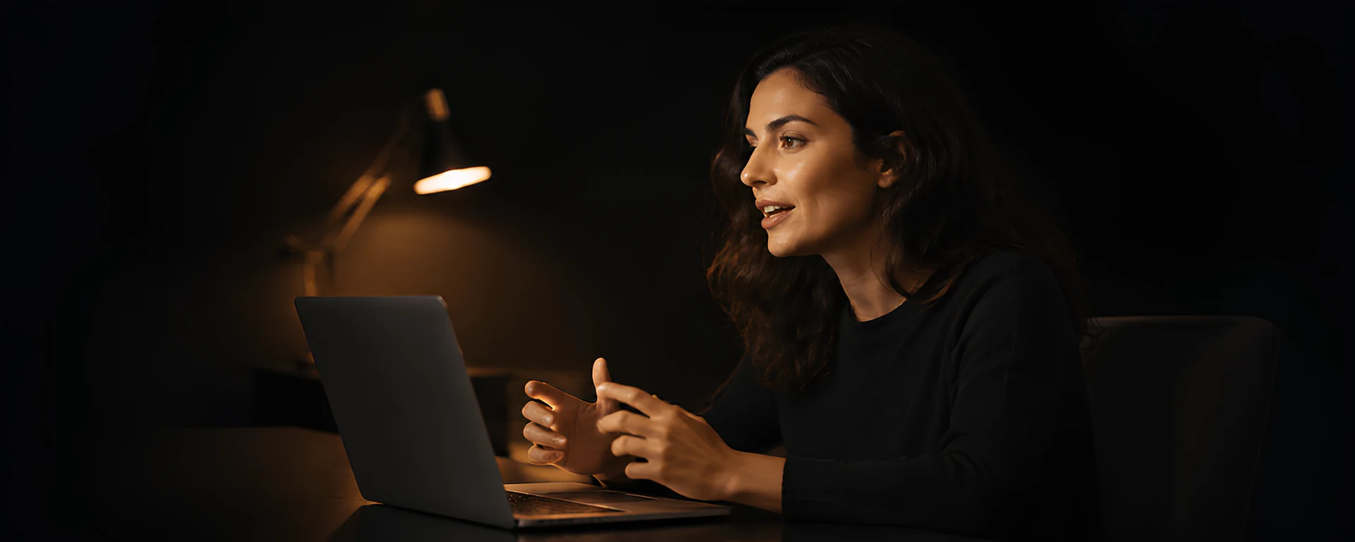 A person speaking naturally while seated at their laptop in warm golden light